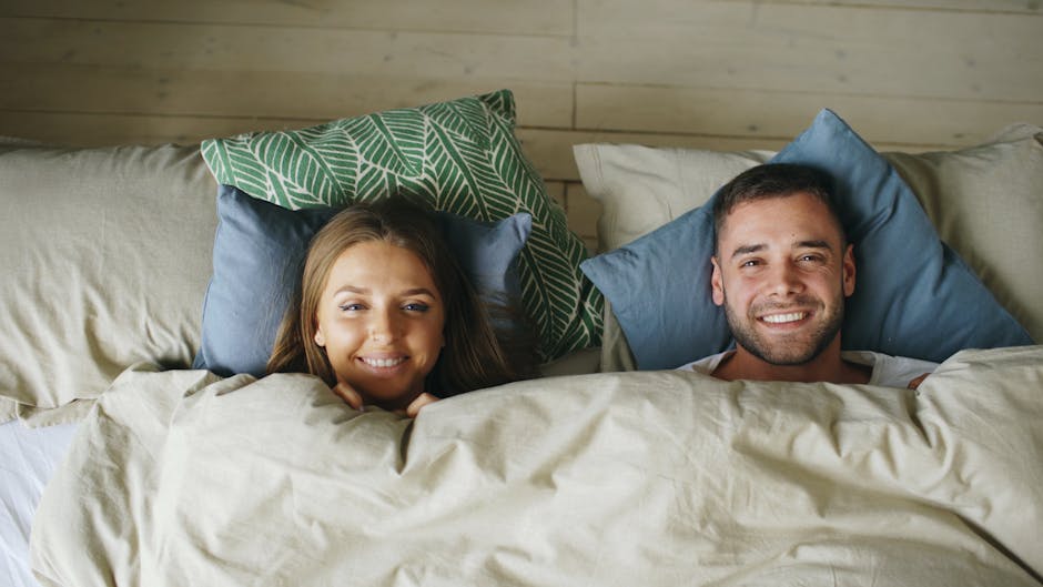 Cheerful couple smiling while relaxing together under cozy linens.